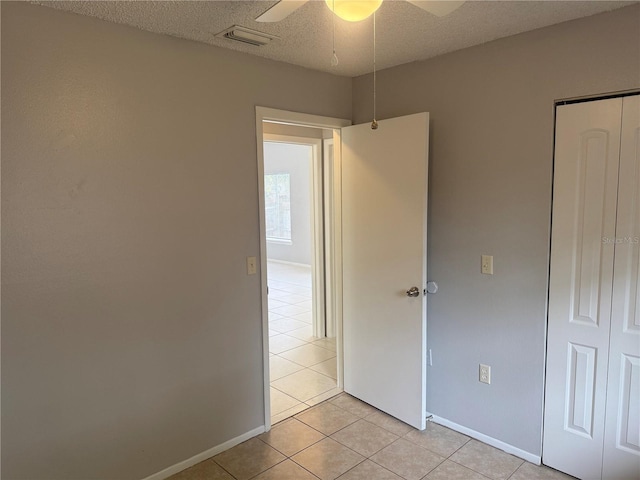 unfurnished bedroom with visible vents, a closet, light tile patterned flooring, a textured ceiling, and a ceiling fan