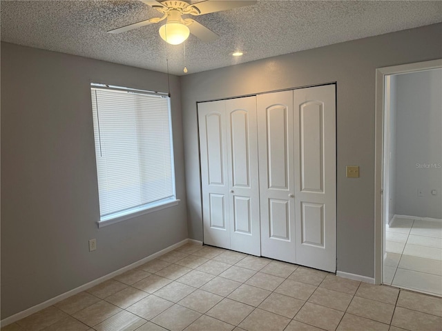 unfurnished bedroom with baseboards, ceiling fan, a closet, light tile patterned flooring, and a textured ceiling