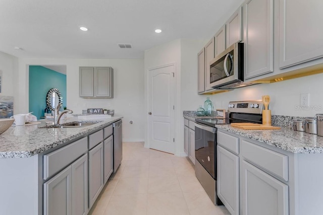 kitchen with stainless steel appliances, a kitchen island with sink, sink, gray cabinets, and light tile patterned flooring