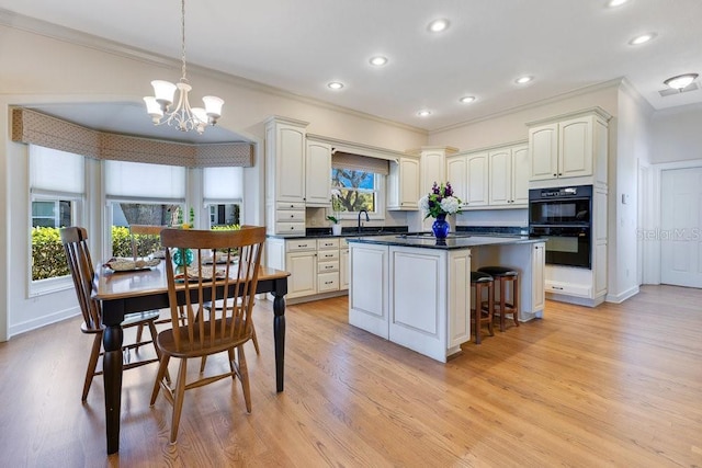 kitchen with decorative light fixtures, ornamental molding, a chandelier, double oven, and light hardwood / wood-style flooring