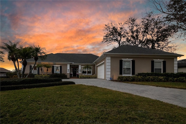 view of front facade featuring a garage, stucco siding, decorative driveway, and a yard