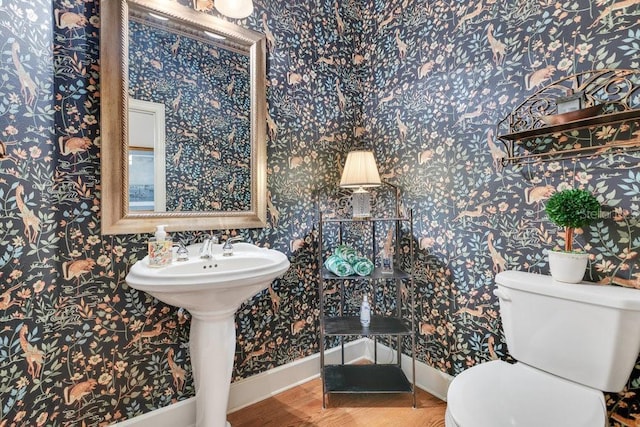 half bathroom with toilet, wallpapered walls, baseboards, and wood finished floors