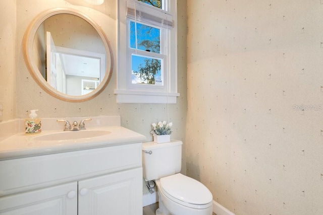 half bath with toilet, vanity, and wallpapered walls