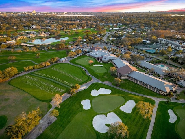 aerial view at dusk featuring a water view and golf course view