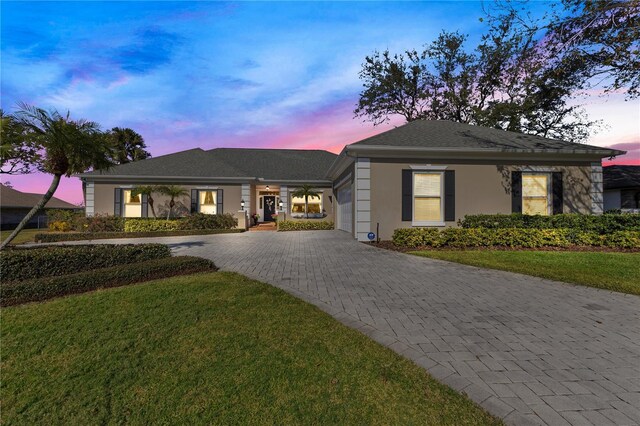 view of front of house featuring a garage, stucco siding, decorative driveway, and a yard