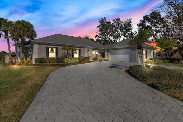 ranch-style house with decorative driveway, a lawn, an attached garage, and stucco siding