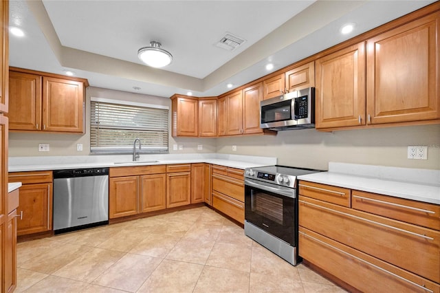 kitchen featuring sink, stainless steel appliances, light tile patterned floors, and a tray ceiling