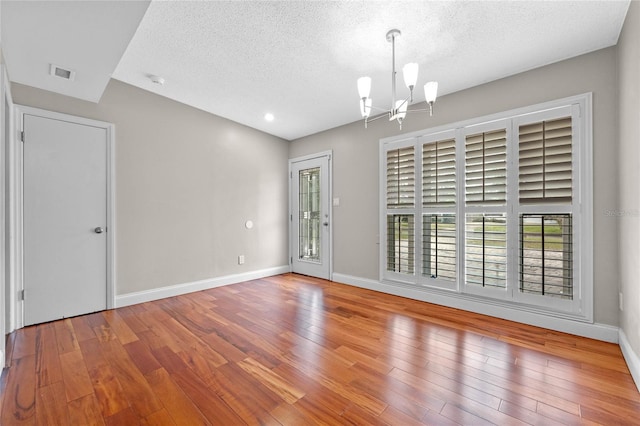 unfurnished room featuring a textured ceiling, a chandelier, and wood-type flooring