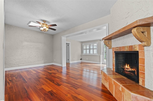 unfurnished living room with ceiling fan, a tile fireplace, a textured ceiling, and wood-type flooring