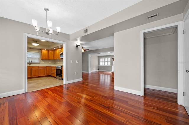 unfurnished living room featuring ceiling fan with notable chandelier, a textured ceiling, sink, and light hardwood / wood-style floors