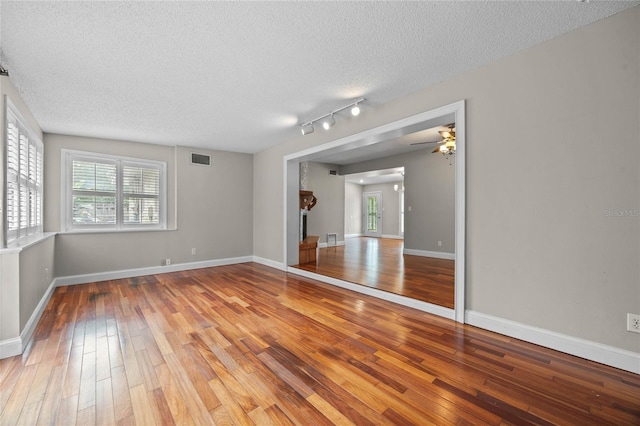 empty room featuring track lighting, ceiling fan, a textured ceiling, and wood-type flooring