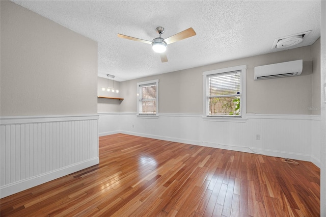 unfurnished room with a wall mounted AC, ceiling fan, light hardwood / wood-style floors, and a textured ceiling