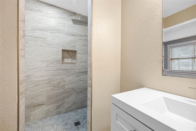 bathroom featuring a textured ceiling, tiled shower, and vanity