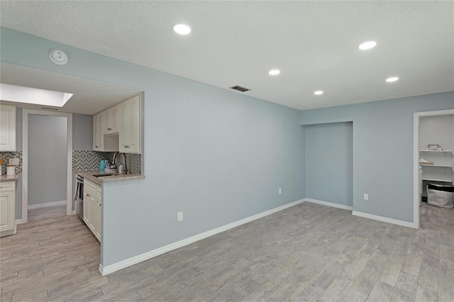 kitchen with tasteful backsplash, sink, a textured ceiling, and light hardwood / wood-style flooring