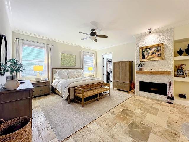 bedroom featuring a stone fireplace, crown molding, ceiling fan, a spacious closet, and a closet