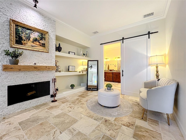 sitting room featuring a barn door, built in features, crown molding, and a stone fireplace