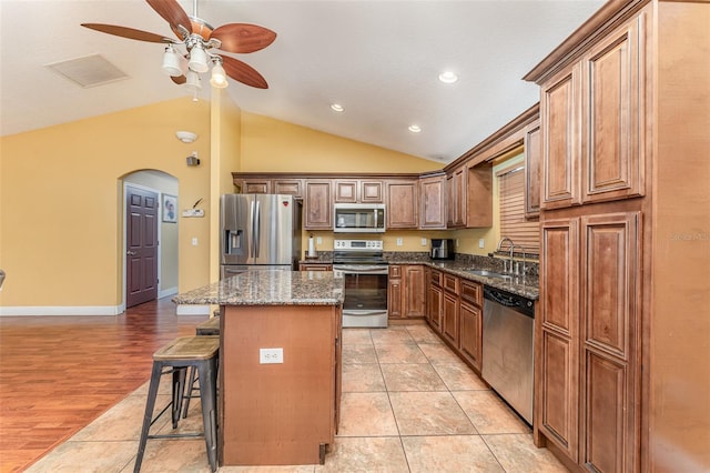 kitchen with stainless steel appliances, light tile patterned floors, a kitchen island, lofted ceiling, and sink