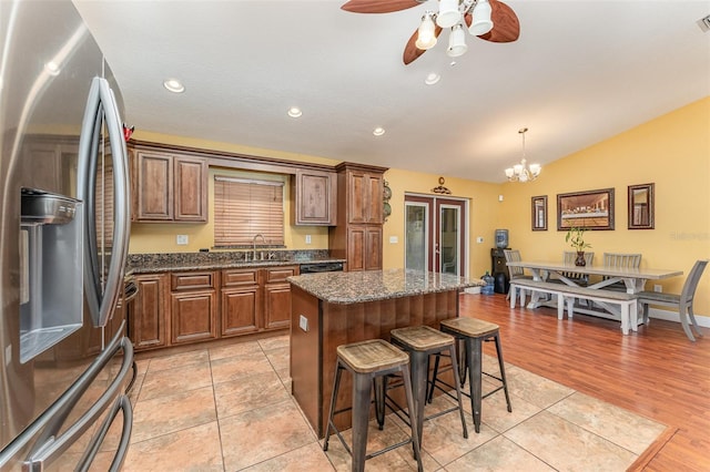 kitchen with stainless steel fridge with ice dispenser, a breakfast bar, a kitchen island, decorative light fixtures, and ceiling fan with notable chandelier