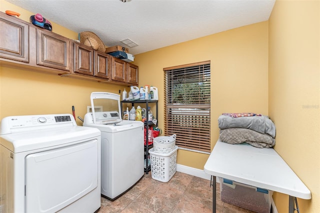 laundry area with washing machine and dryer, a textured ceiling, and cabinets