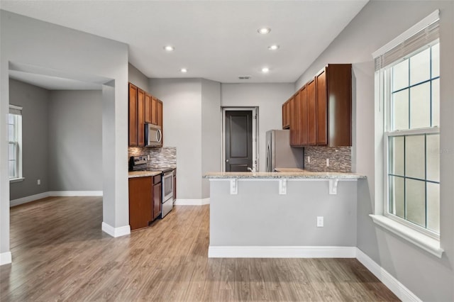 kitchen with stainless steel appliances, kitchen peninsula, a kitchen bar, decorative backsplash, and light wood-type flooring