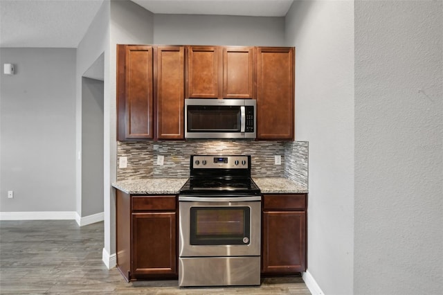 kitchen featuring hardwood / wood-style flooring, light stone counters, appliances with stainless steel finishes, and tasteful backsplash