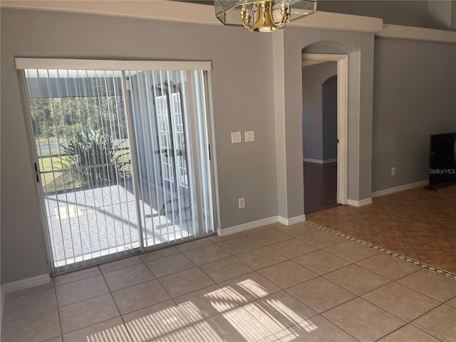 tiled spare room with a notable chandelier