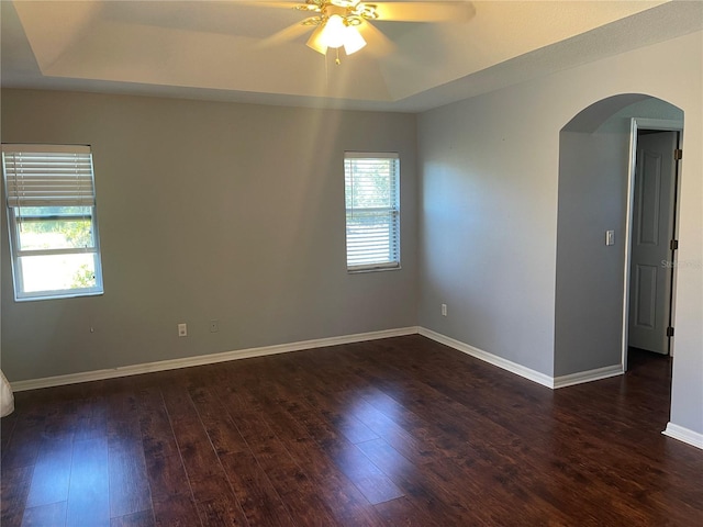 spare room with dark hardwood / wood-style flooring, a raised ceiling, and ceiling fan