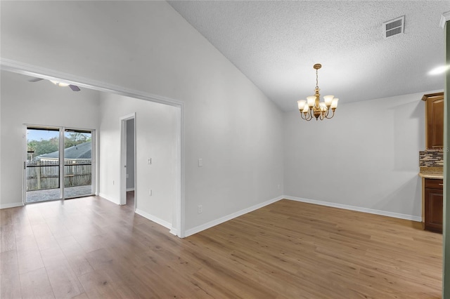 unfurnished dining area with lofted ceiling, light hardwood / wood-style floors, a textured ceiling, and a notable chandelier