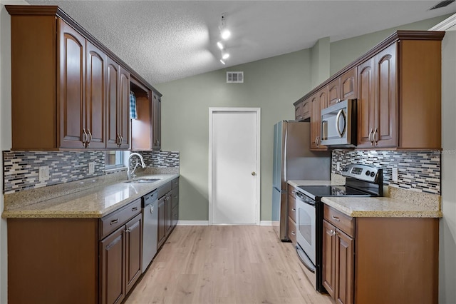 kitchen featuring lofted ceiling, sink, light hardwood / wood-style flooring, stainless steel appliances, and light stone countertops