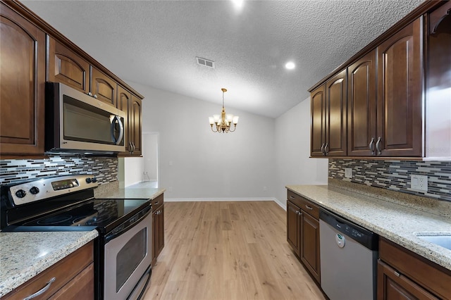 kitchen featuring lofted ceiling, pendant lighting, stainless steel appliances, light stone counters, and light wood-type flooring