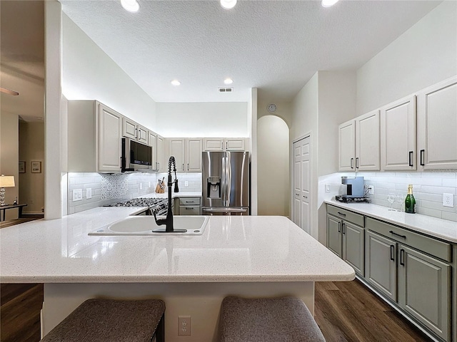 kitchen with arched walkways, a breakfast bar area, gray cabinetry, a peninsula, and appliances with stainless steel finishes