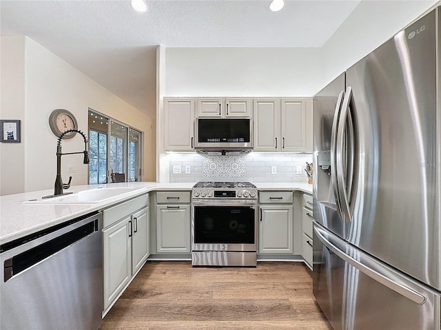 kitchen featuring a sink, stainless steel appliances, light countertops, light wood-type flooring, and backsplash