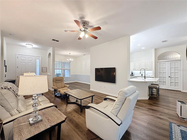 living room featuring ceiling fan with notable chandelier, dark wood finished floors, and visible vents