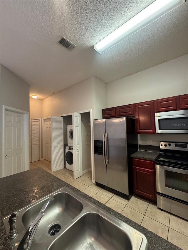 kitchen with appliances with stainless steel finishes, a textured ceiling, sink, light tile patterned floors, and stacked washer and clothes dryer