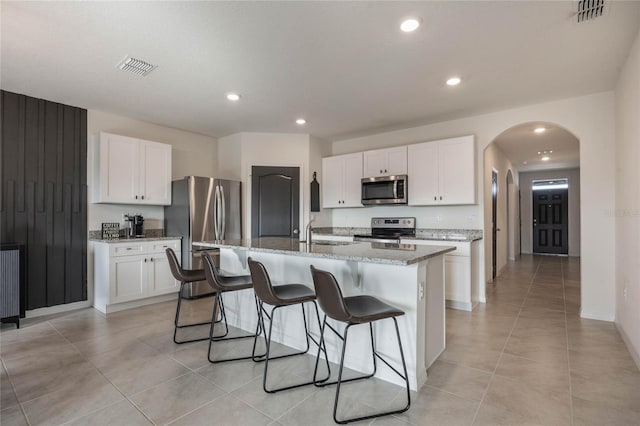 kitchen with white cabinets, stainless steel appliances, a kitchen island with sink, and light stone counters