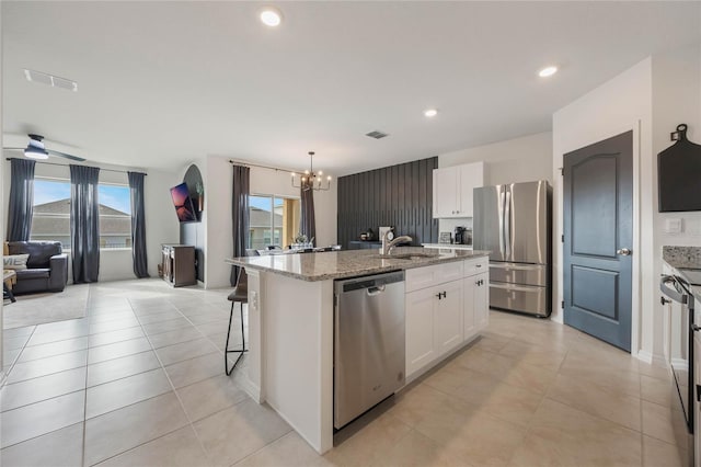 kitchen featuring stainless steel appliances, a center island with sink, white cabinets, and pendant lighting