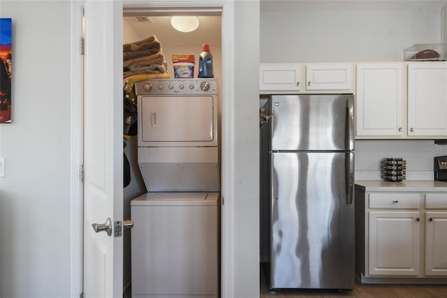 kitchen with stacked washer / dryer, white cabinets, and stainless steel fridge