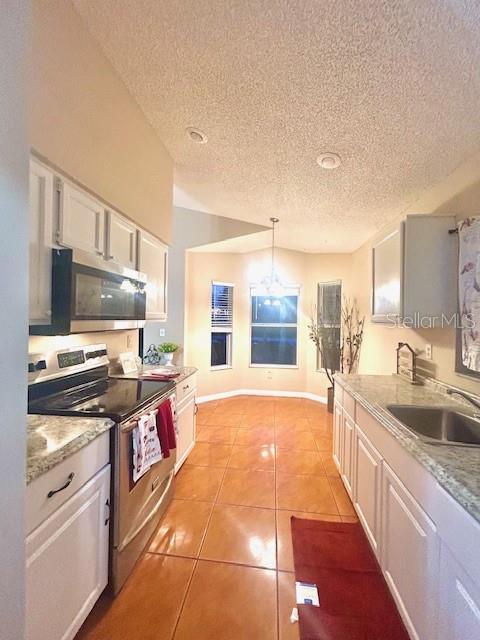 kitchen featuring stainless steel appliances, light tile patterned floors, white cabinets, and decorative light fixtures