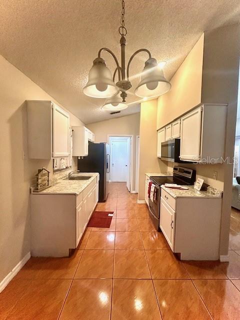 kitchen with vaulted ceiling, appliances with stainless steel finishes, sink, white cabinets, and tile patterned floors