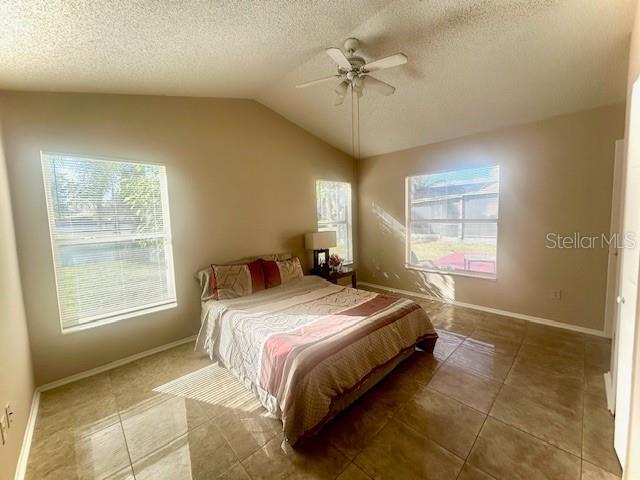 tiled bedroom featuring lofted ceiling, a textured ceiling, and ceiling fan