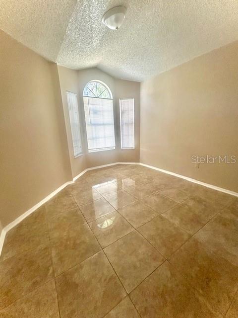 spare room featuring tile patterned floors, lofted ceiling, and a textured ceiling