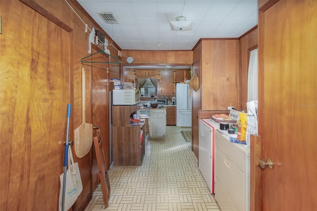 kitchen featuring pendant lighting, white appliances, washer and clothes dryer, and wood walls