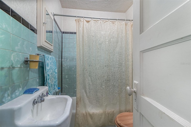 full bathroom with toilet, sink, tile walls, a textured ceiling, and shower / bath combo with shower curtain