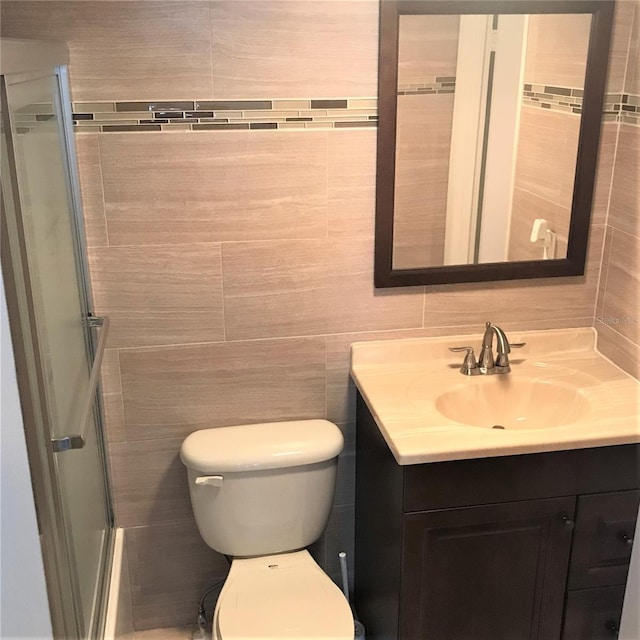 bathroom featuring vanity, toilet, walk in shower, and tile walls