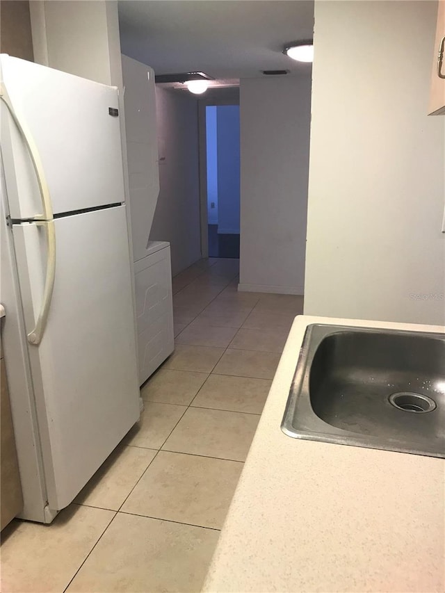 kitchen with white fridge, washer / dryer, light tile patterned floors, and sink