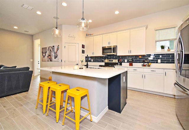 kitchen featuring a center island with sink, white cabinets, a breakfast bar area, decorative light fixtures, and stainless steel appliances