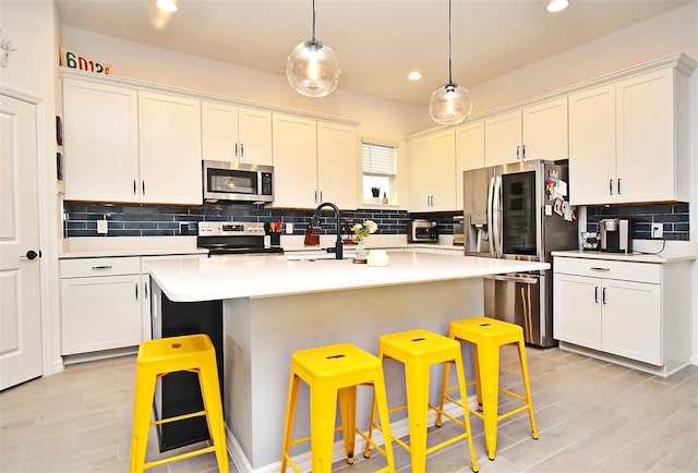 kitchen featuring hanging light fixtures, an island with sink, a breakfast bar area, white cabinets, and appliances with stainless steel finishes