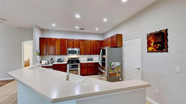 kitchen with appliances with stainless steel finishes, kitchen peninsula, sink, and light tile patterned floors