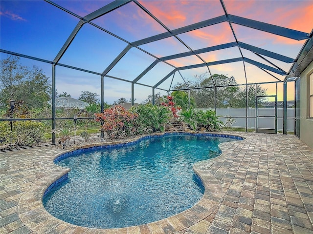 pool at dusk featuring glass enclosure and a patio area