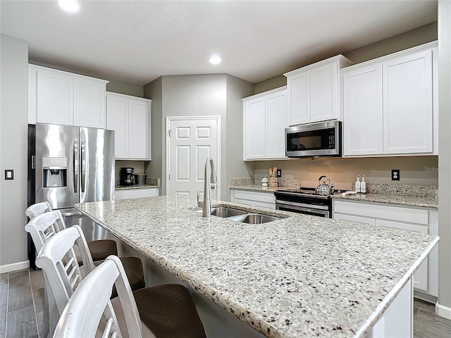 kitchen with light stone countertops, sink, a center island with sink, white cabinets, and appliances with stainless steel finishes